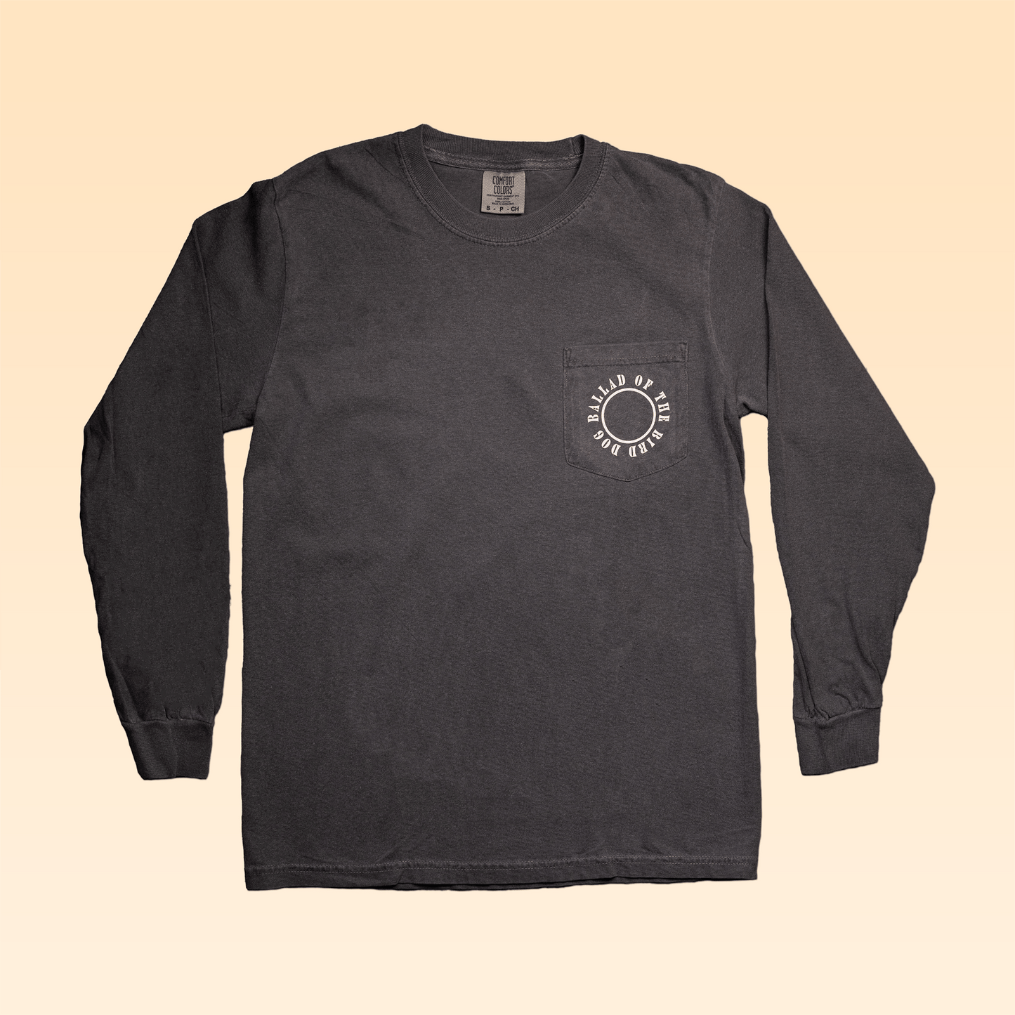 The Long Sleeve Pocket Shirt | Thunderbird by Ballad of the Bird Dog features a chest pocket with a circular white graphic and text on dark gray fabric, styled flat on a beige gradient—your ideal adventure shirt.
