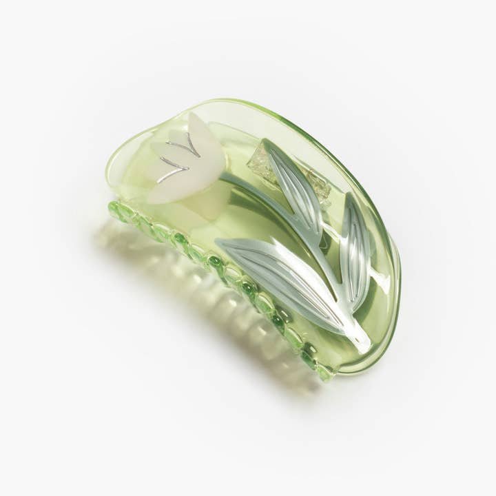 The Winona Irene Lotus Flower Hair Claw in clear green acetate features a delicate white tulip with green leaves, inspired by the vibrant paddle boats at Echo Park’s Lotus Festival.