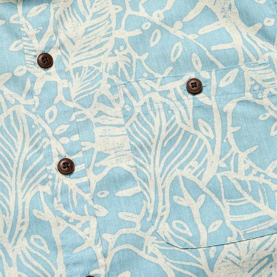 Close-up of the Mansfield Shirt | Leafy Lithographs by Howler Brothers, showing its button-down collar, lightweight cotton-poly blend in light blue with a white leafy print, brown buttons, and a front pocket.