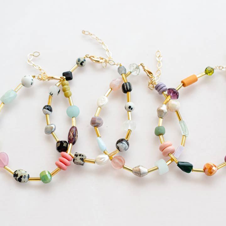 Four Mariposa Bracelets by Jill Makes, featuring colorful gemstone beads and gold adjustable chain extenders, are displayed on a white background.