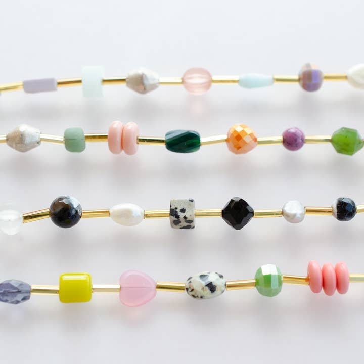 The Mariposa Bracelet by Jill Makes features four gold wires strung with colorful, uniquely shaped gemstone beads arranged in parallel rows, creating an elegant accessory.