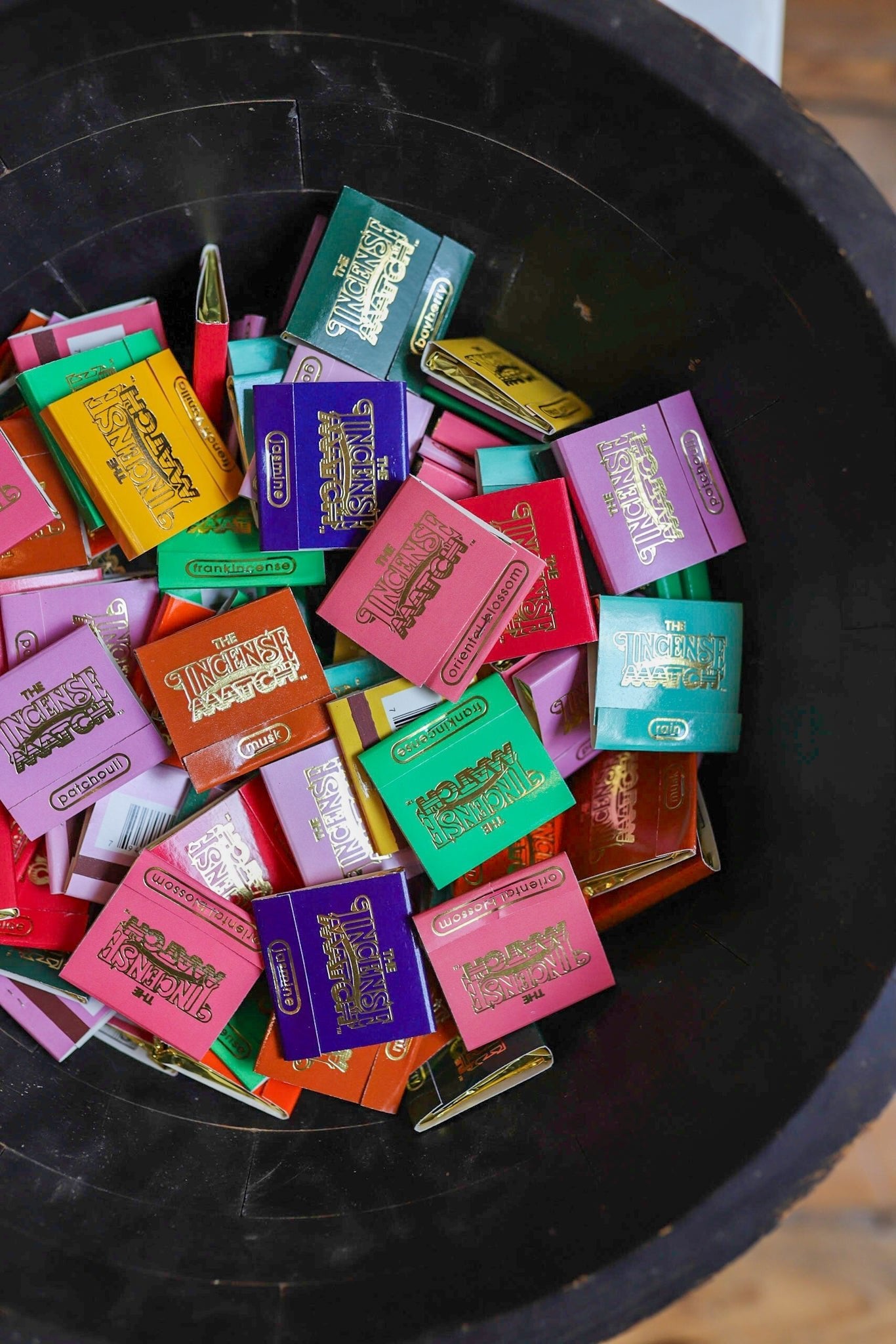 A black bowl holds colorful “Matches | The Incense Match” by The Incense Match, each pack combining fragrance and style—a portable incense match that freshens any space, making it a unique scented gift or air freshener.