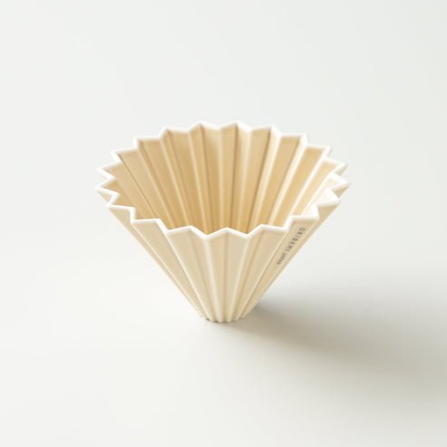 The Medium Dripper by Origami Japan is a cream-colored, pleated ceramic pour-over coffee dripper with a fluted design, shown resting on a plain white surface.