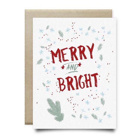 The Merry And Bright Card by Anvil Cards features "Merry and Bright" in red with green pine needles, blue snowflakes, and red dots on linen paper. Includes a brown envelope; blank inside for your message.