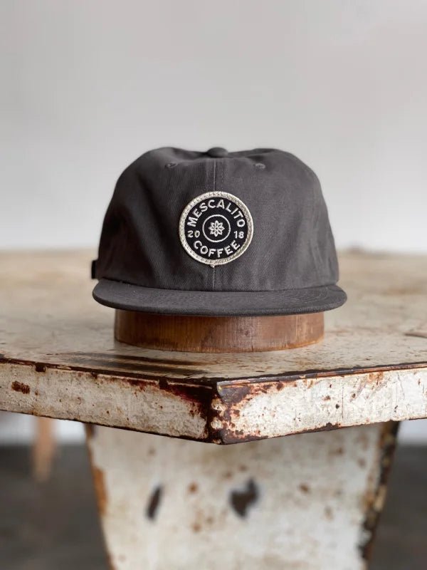 The Mescalito Field Hat by Ballad of the Bird Dog features a round "Mescalito Coffee" patch on dark gray cotton—your ideal go-to coffee shop cap.