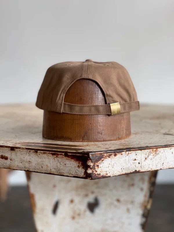 The Mescalito Field Hat by Ballad of the Bird Dog for Mescalito Coffee is shown backward on a wooden stand placed on a worn, white metal table.