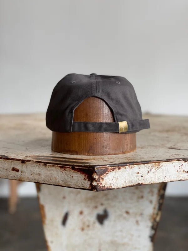 The Mescalito Field Hat by Ballad of the Bird Dog is shown backwards on a wooden hat block on a weathered white metal table—an ideal pick for Mescalito Coffee fans or anyone looking for the perfect coffee shop hat.