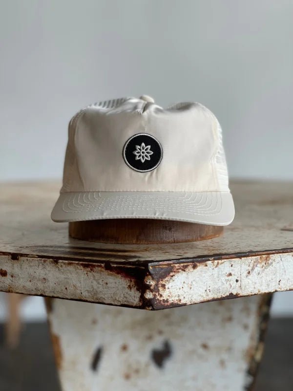 The Mescalito Nylon Field Hat by Ballad of the Bird Dog features a beige nylon build and black patch with a white atomic emblem—an ideal accessory for any Mescalito Coffee visit.
