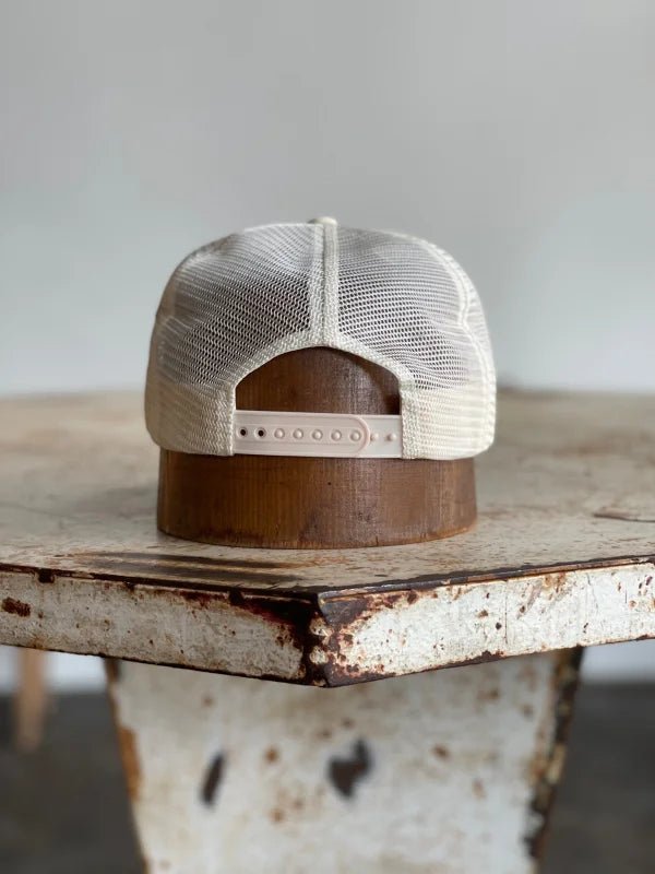 The Ballad of the Bird Dog Mescalito Nylon Field Hat from Mescalito Coffee is shown backwards on a weathered wooden table with a distressed white surface.