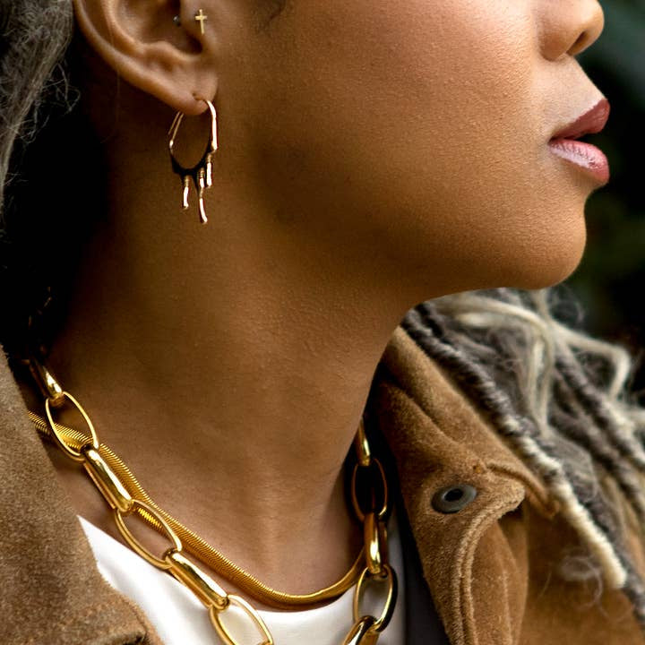 A person in a brown jacket and 24k gold-plated hoop earrings wears the "Pretty in Link 24k Gold Plated Necklace" by Peter and June, shown in a close-up side profile.