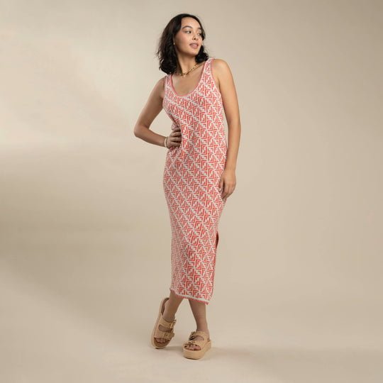 A woman stands on a neutral background wearing the Sendero Provisions Co. Puebla Knit Dress, a sleeveless, ankle-length dress with a red and white pattern, styled with beige platform sandals.
