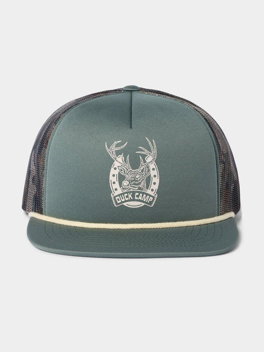 The Duck Camp Lucky Deer Hat is a green trucker hat with mesh back, rope brim detail, and a white front logo with antlers and horseshoe. It features an adjustable snapback for comfort.
