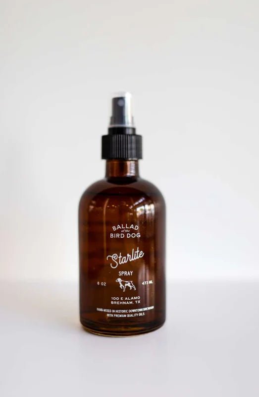 An 8 oz (473 ml) brown glass spray bottle labeled "Room & Linen Spray | Starlite Serenade" by Ballad of the Bird Dog, handcrafted in Brenham, Texas with essential oils and a black nozzle, is shown against a plain white background.