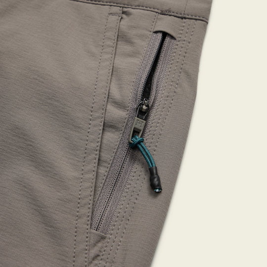 Close-up of Shoalwater Tech Shorts by Howler Brothers in gray, highlighting the 4-way stretch nylon pocket with a vertical zipper and teal and black pull cord.