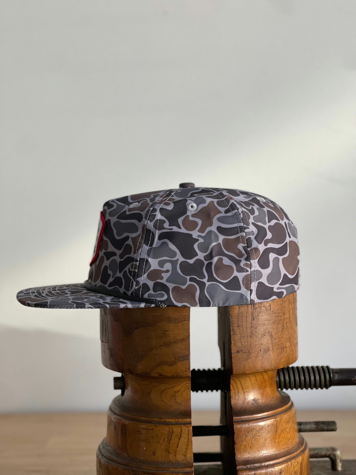 The Ballad of the Bird Dog Shop Hat | Camo Companion is shown on a wooden hat press against a plain background—perfect outdoor headwear for stylish camouflage.