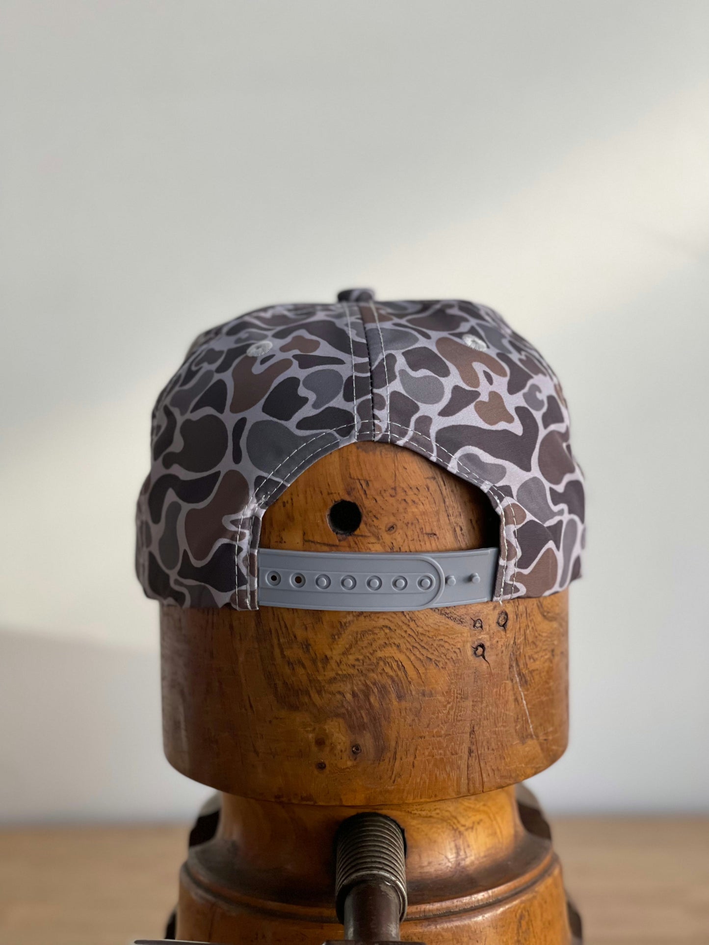 The Ballad of the Bird Dog Shop Hat | Camo Companion features a gray snapback with a black and white Smoke Show Camo pattern, displayed backward on a wooden mannequin—perfect for any outdoor adventure.