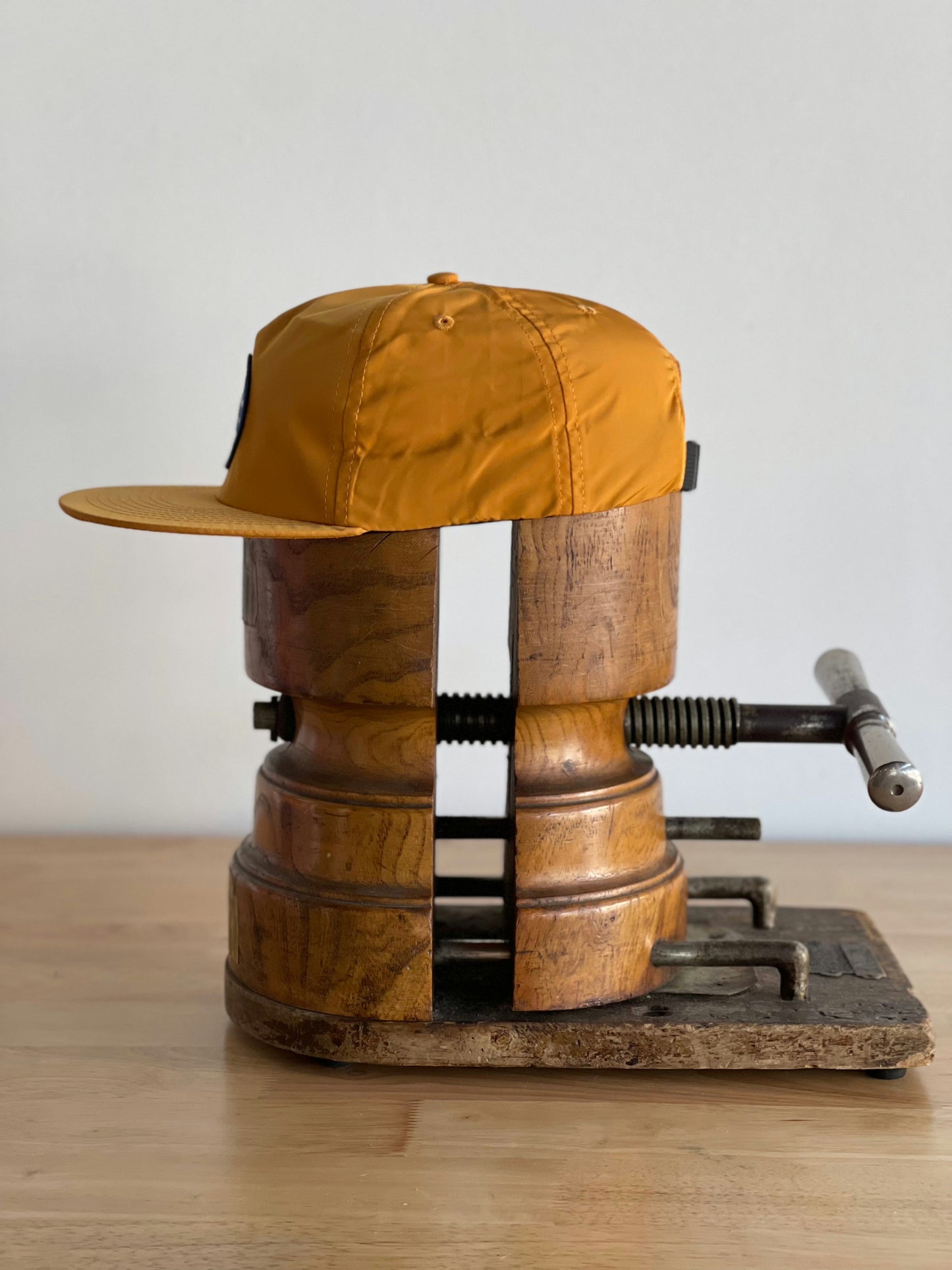 The Shop Hat | Circle Clubhouse Tradition by Ballad of the Bird Dog is displayed on a wooden hat stretcher with a metal crank, resting on a wooden surface against a plain background.