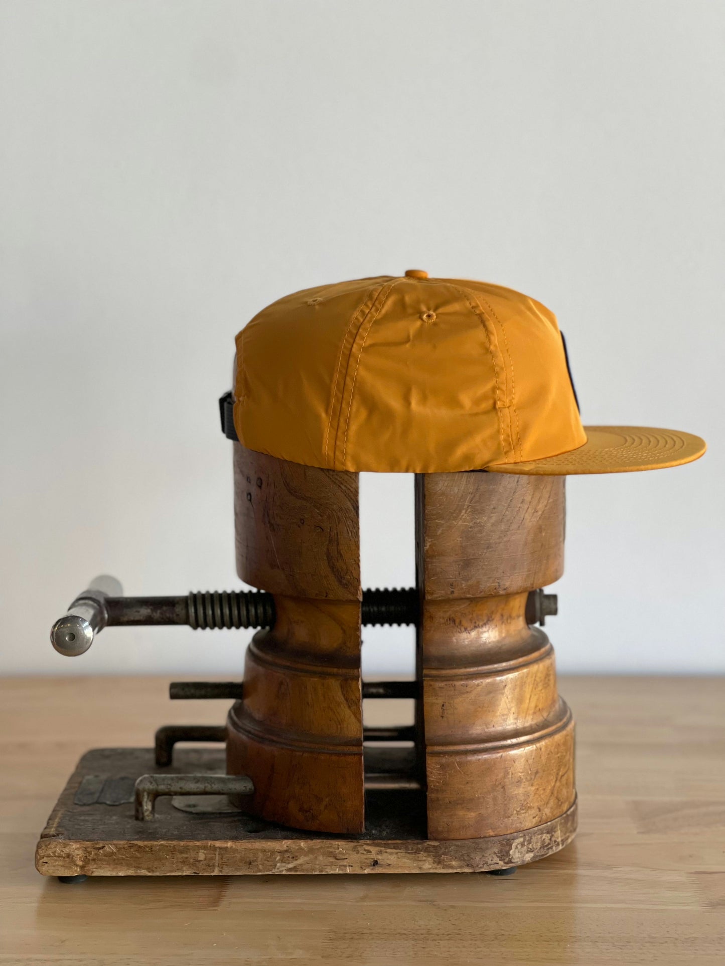 A Ballad of the Bird Dog Shop Hat | Circle Clubhouse Tradition is held between two wooden blocks in a metal vise on a wooden surface.