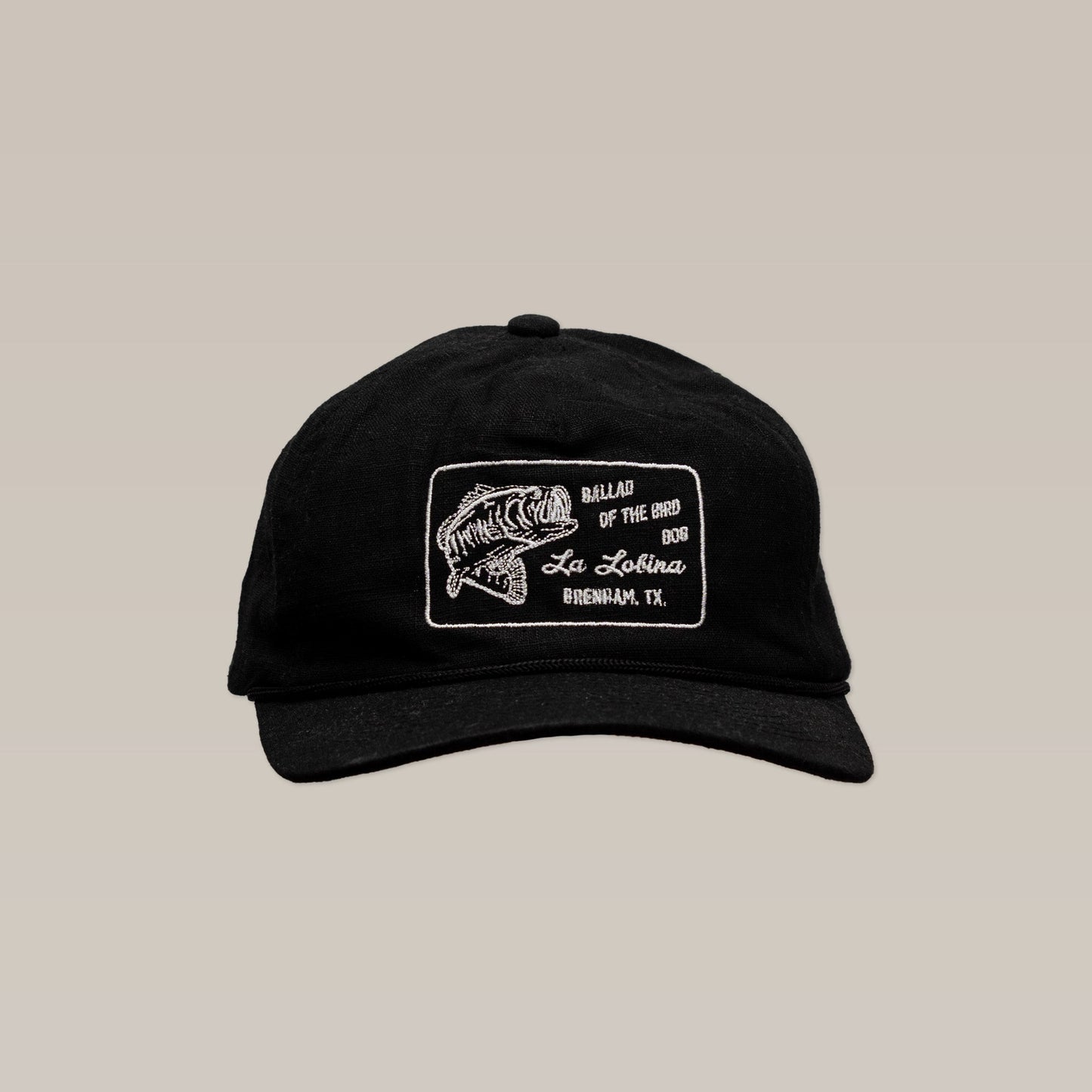The Shop Hat | La Lobina by Ballad of the Bird Dog is a black angler hat with a white embroidered fish patch and text: "Ballad of the Big Bass, La Lobina Bass Fishing Hat, Brenham, TX.
