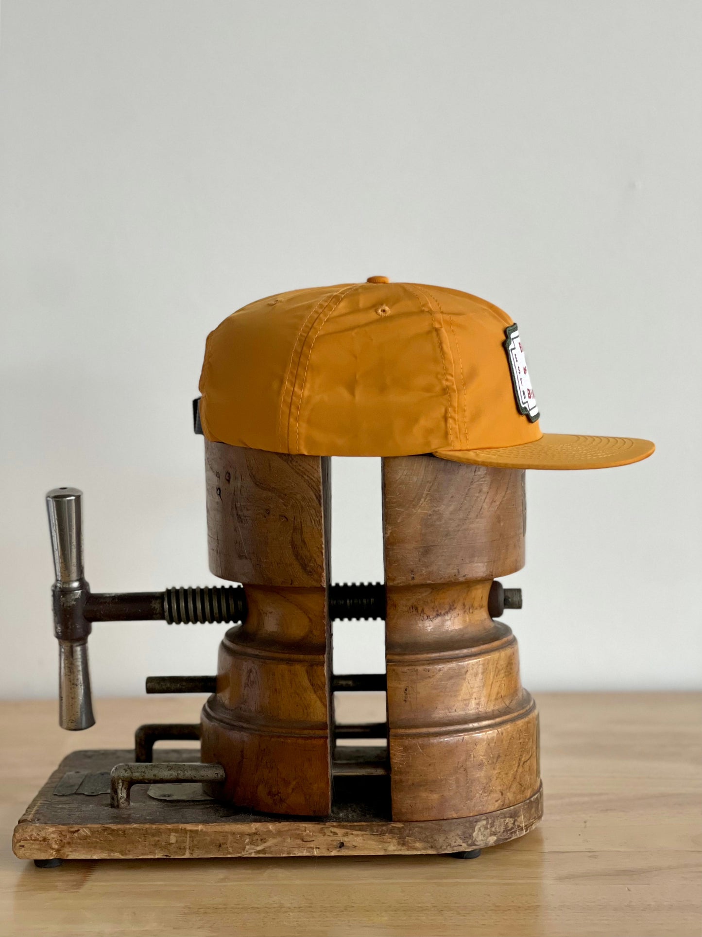 A Shop Hat by Ballad of the Bird Dog is held in a vintage wooden hat stretcher on a wooden surface in downtown Brenham.