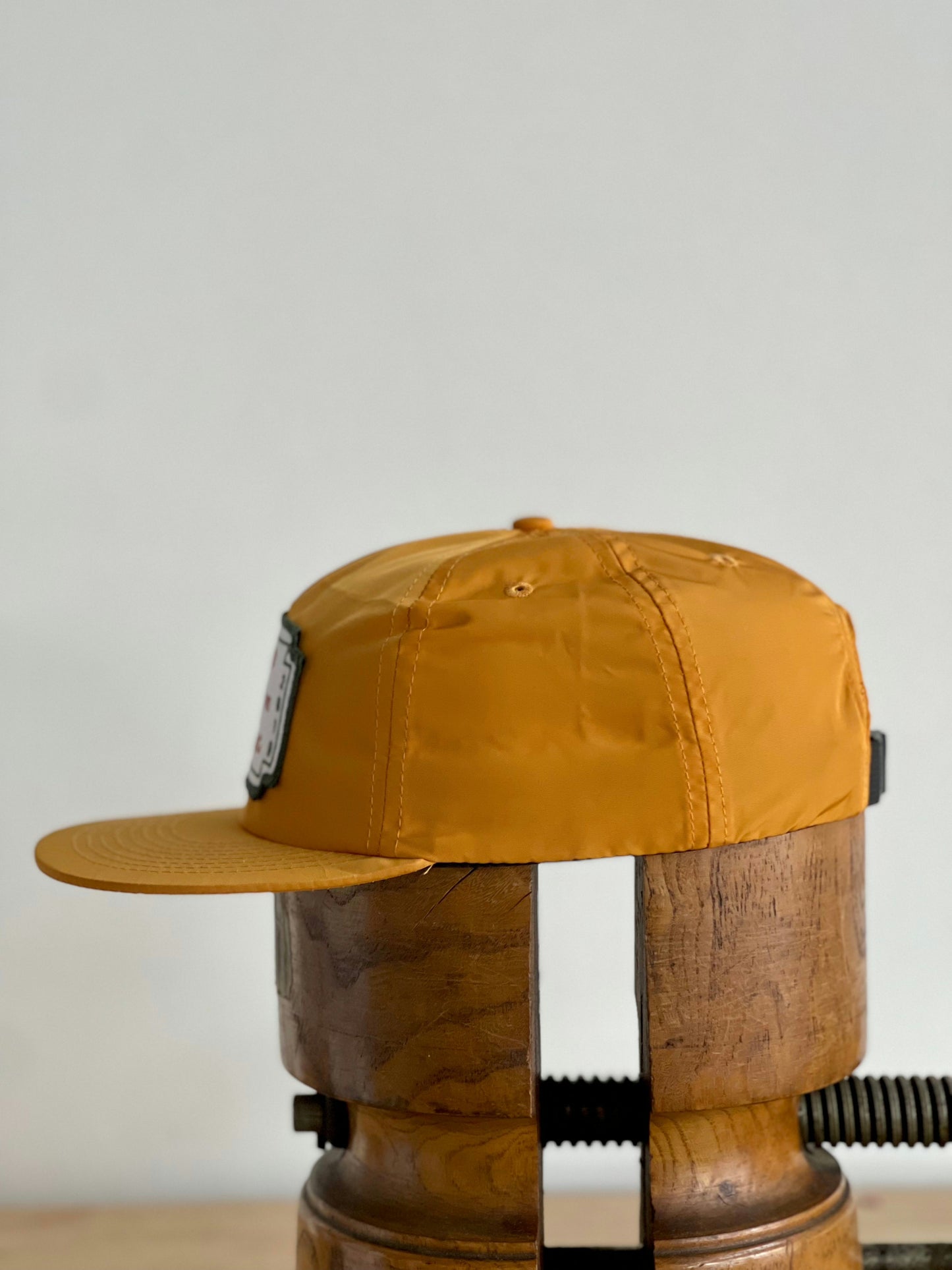 The Shop Hat | Neon Revival by Ballad of the Bird Dog, shown side-on atop a wooden stand with a plain light background, channels relaxed downtown Brenham style in striking mustard yellow with a classic logo.