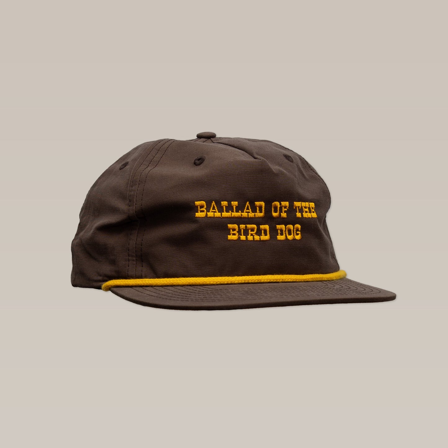 The Shop Hat | Old Fashioned by Ballad of the Bird Dog features a brown design with yellow "BALLAD OF THE BIRD DOG" embroidery and a yellow cord above the brim, channeling classic Wild West style. Shown against a plain background.