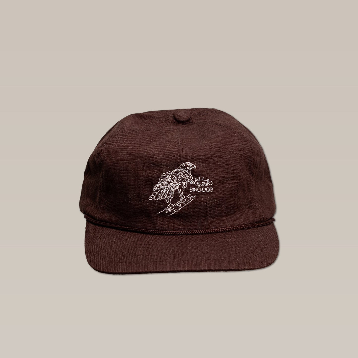 The Shop Hat by Ballad of the Bird Dog is a brown baseball cap featuring an embroidered red-tailed hawk perched on a branch, shown against a plain beige background.