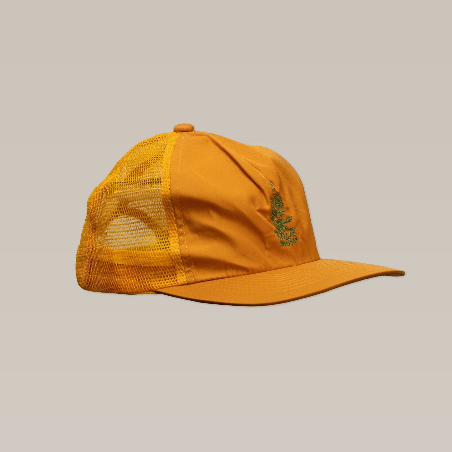 The Shop Hat | Roadrunner Saguaro by Ballad of the Bird Dog is an orange mesh-back trucker hat with a flat brim and green embroidered front graphics, displayed here on a plain beige background.