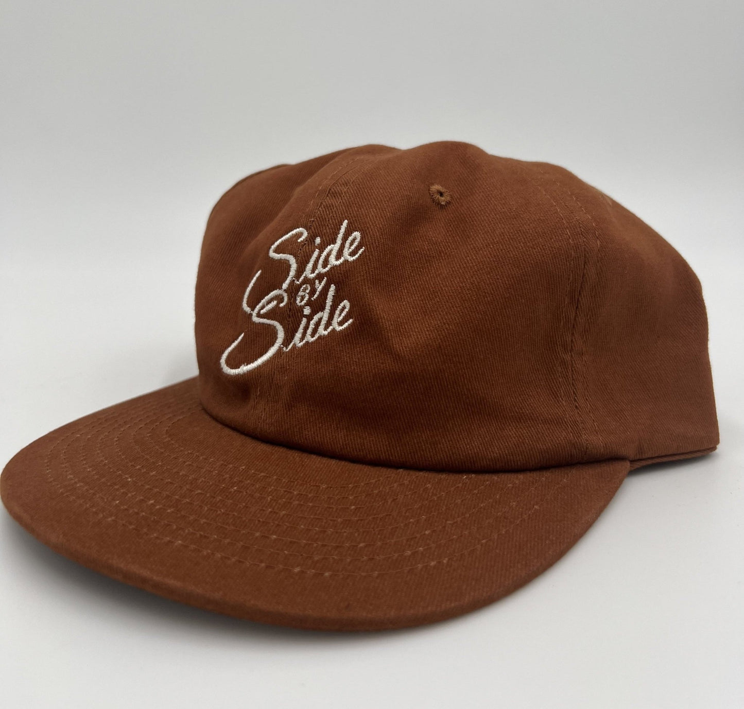 The Ballad of the Bird Dog Shop Hat | Side by Side features "Side by Side" embroidered in white on brown, celebrating bird dog companionship, shown against a plain white background.