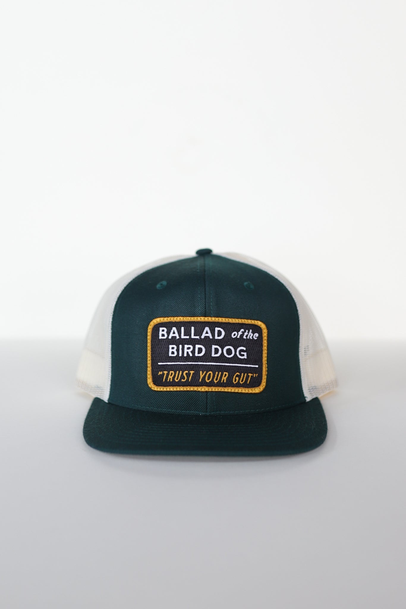 The Shop Hat | Trust Your Gut Vintage Slate by Ballad of the Bird Dog features a green and white mesh design, a front patch with bold yellow "Ballad of the Bird Dog" and "Trust Your Gut," nodding to Brenham Local Hat favorites.