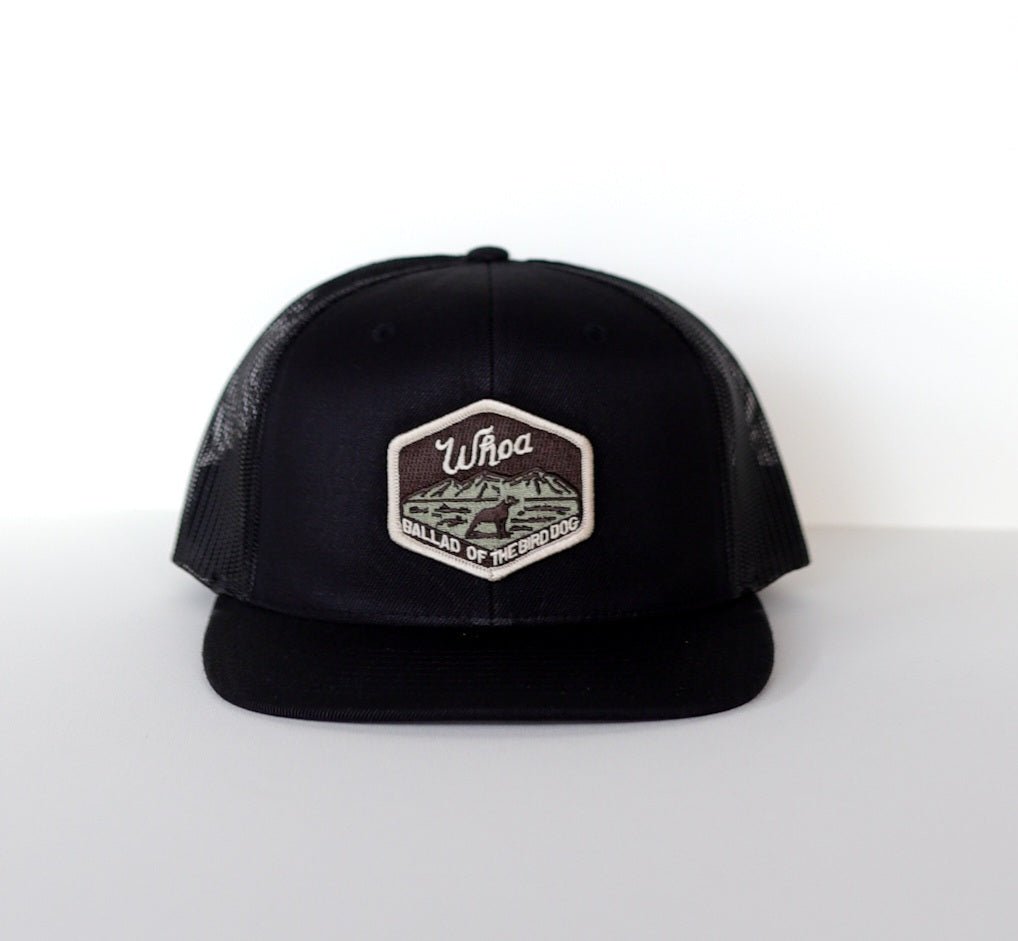 The Shop Hat | Whoa by Ballad of the Bird Dog is a black mesh patch hat with a front hexagonal patch displaying "Whoa Ballad of the Bird Dog" and a bird dog illustration.