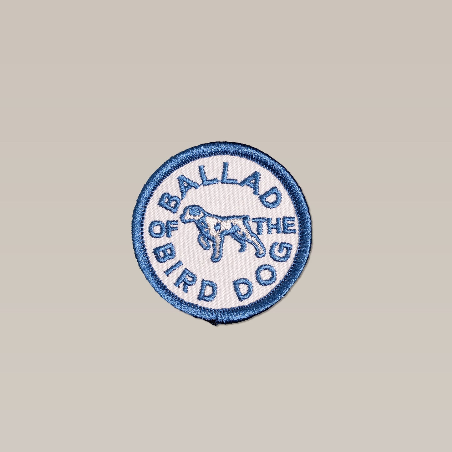 The Shop Patch | Clubhouse Tradition by Ballad of the Bird Dog is a round embroidered patch with a blue border, white background, dog illustration, and "Ballad of the Bird Dog" in blue text.