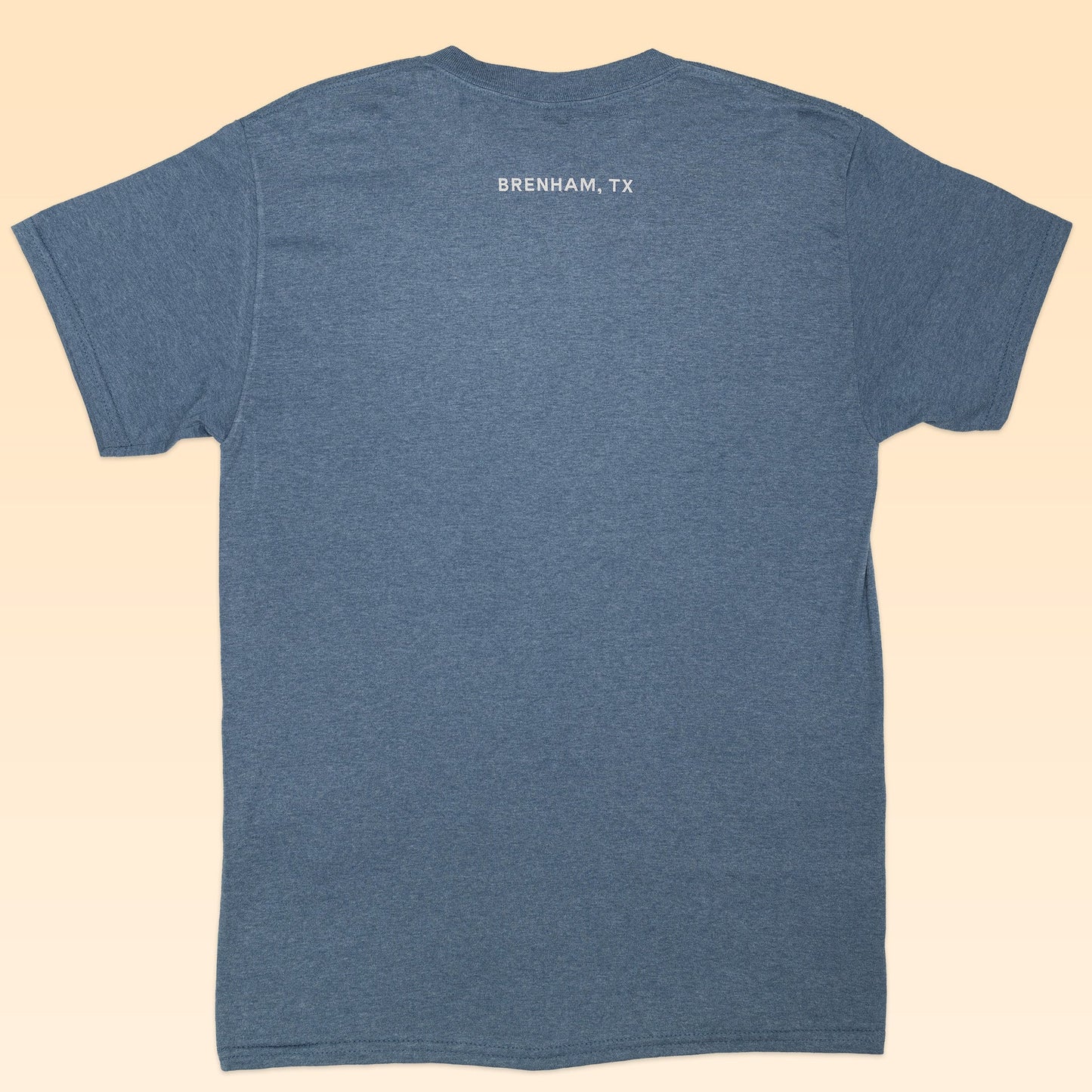 A blue short-sleeve "Shop Shirt | Frontier Oval Logo" from Ballad of the Bird Dog is shown from the back, featuring “BRENHAM, TX” in small white letters near the top—a simple t-shirt ideal for everyday wear.