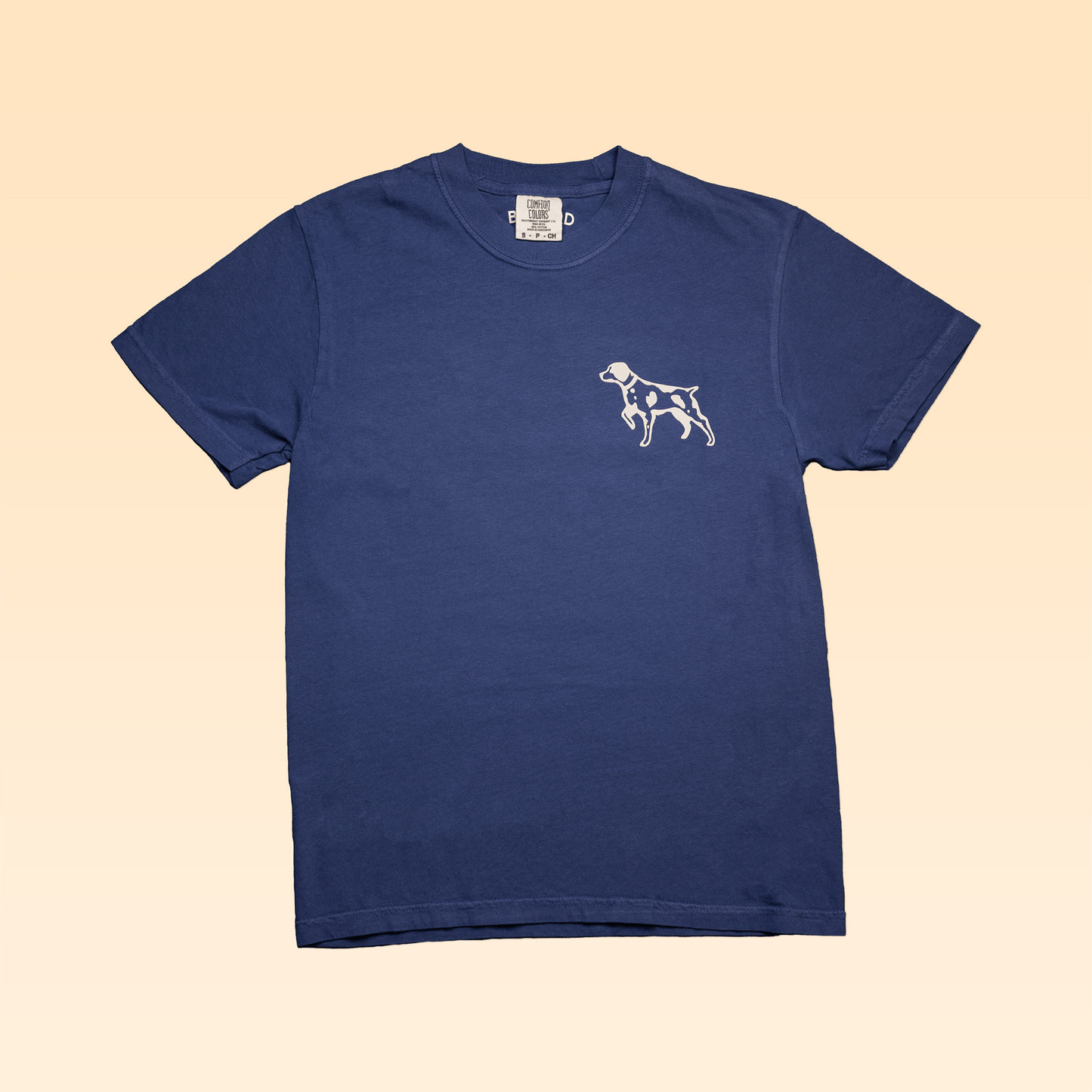 The Ballad of the Bird Dog Shop Shirt | Home Base features a blue Comfort Colors tee with a small white dog graphic on the left chest, displayed flat on a light beige background.