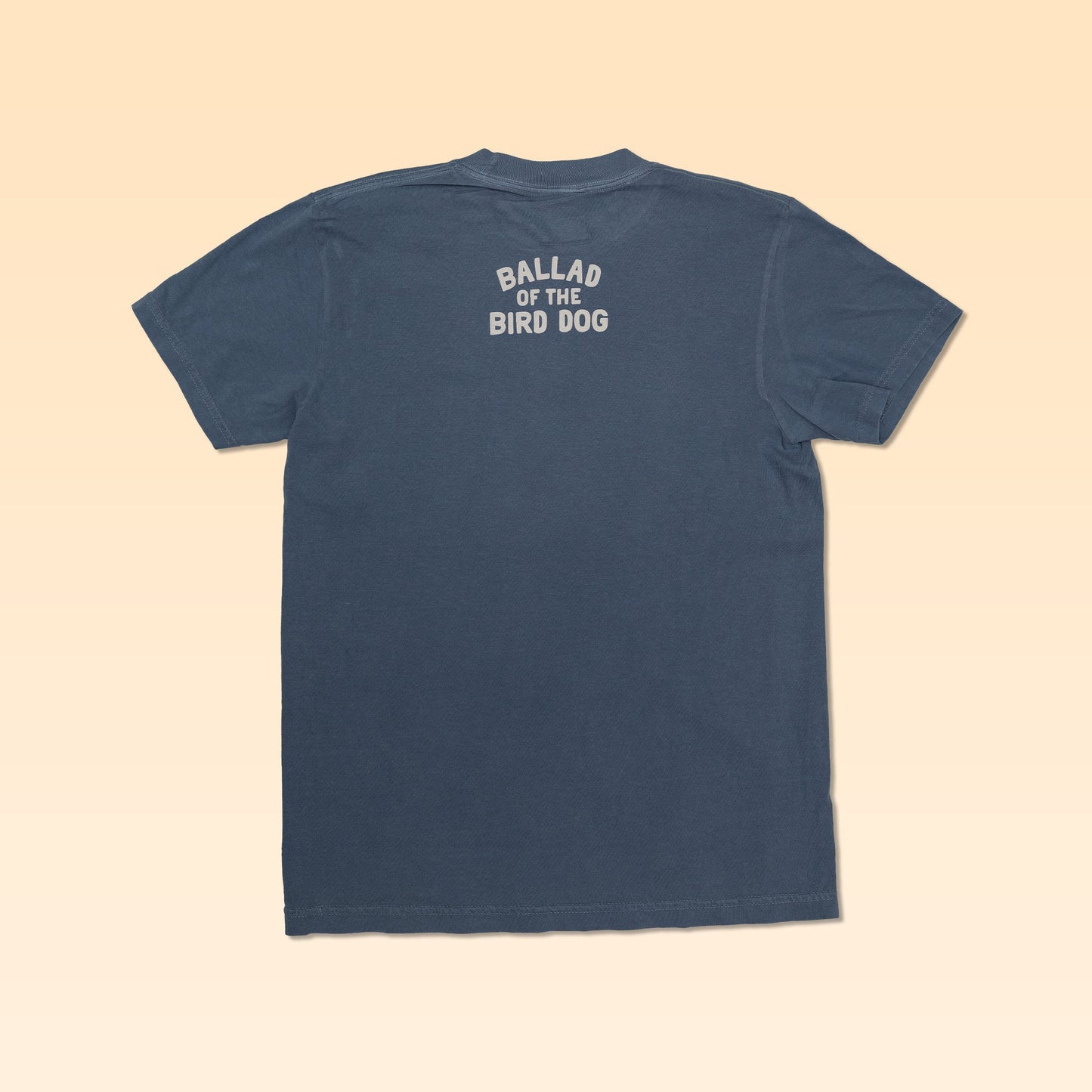 A blue Ballad of the Bird Dog Shop Shirt is laid flat, back up, with "BALLAD OF THE BIRD DOG" printed in white near the neck—a tribute to its Somewhere Texas roots.