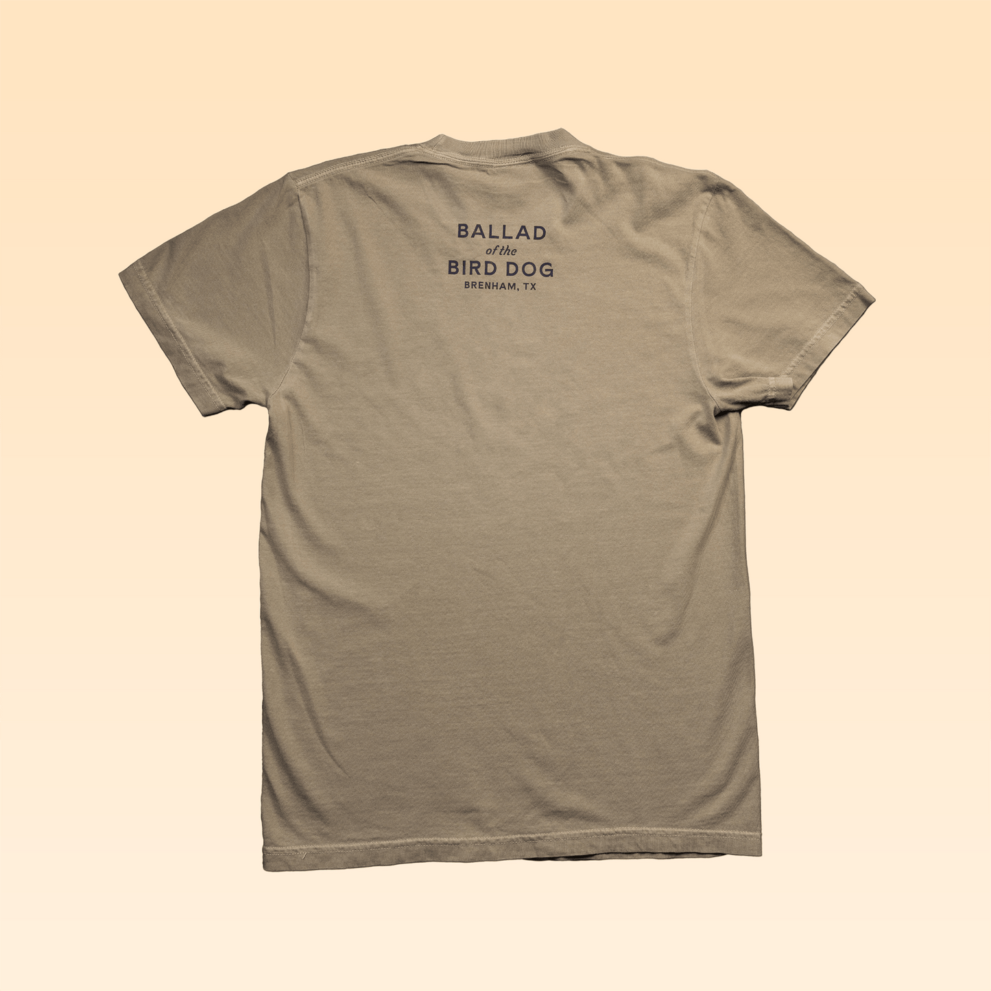 The Shop Shirt | Upland Morning by Ballad of the Bird Dog is shown from the back in beige, featuring "BALLAD of the BIRD DOG BRENHAM, TX" in dark print near the top. Made from soft USA cotton for comfort all day.