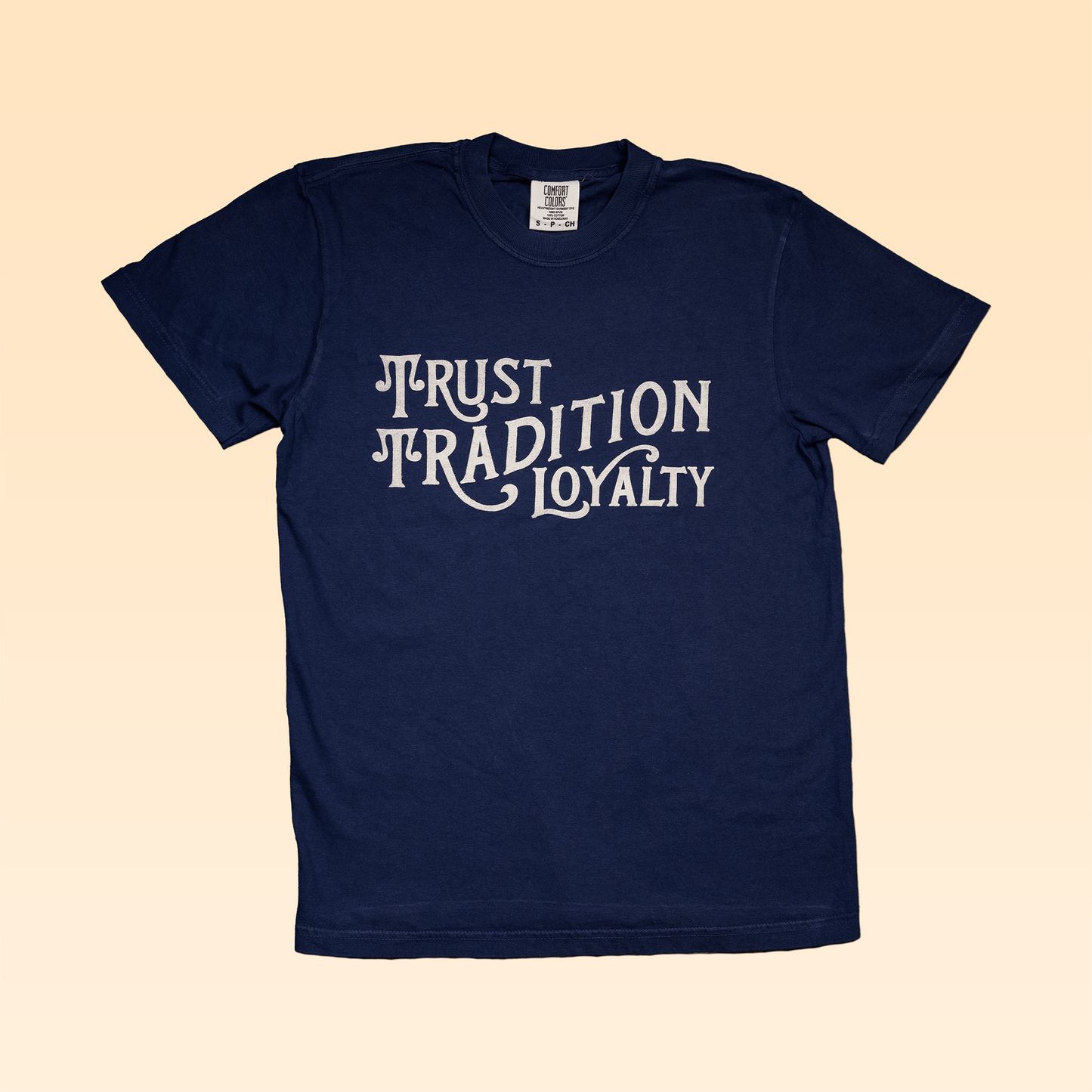 The Shop Shirt | Values by Ballad of the Bird Dog is a navy blue USA cotton tee with "Trust Tradition Loyalty" in white stylized text, shown on a light beige background.