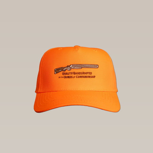 The Side by Side cap by Ballad of the Bird Dog is a bright orange baseball hat with an embroidered shotgun and "QUALITY GOODS ROOTED IN THE BONDS OF COMPANIONSHIP" text on the front.