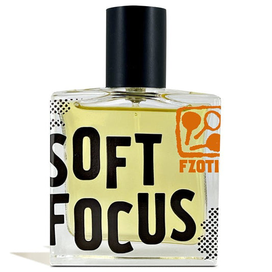A rectangular glass perfume bottle from Fzotic, Soft Focus, with yellow liquid inside and a black cap. "SOFT FOCUS" is printed boldly on the front, while an orange Fzotic logo at the top right suggests a refreshing summer scent.