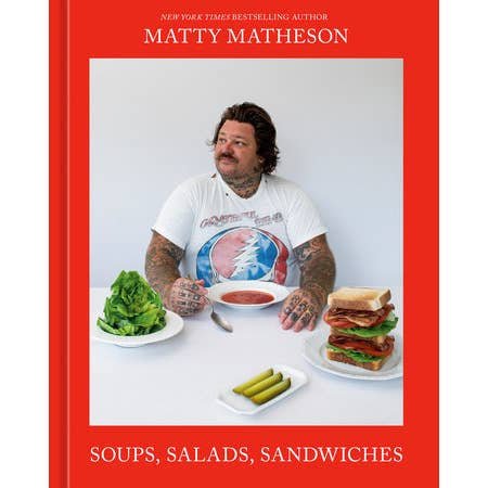 A tattooed man sits at a table with lettuce, soup, pickles, and sandwiches. The cover shows "Soups, Salads, Sandwiches" by Penguin—a Matty Matheson cookbook featuring creative recipes for soups, salads, and sandwiches.
