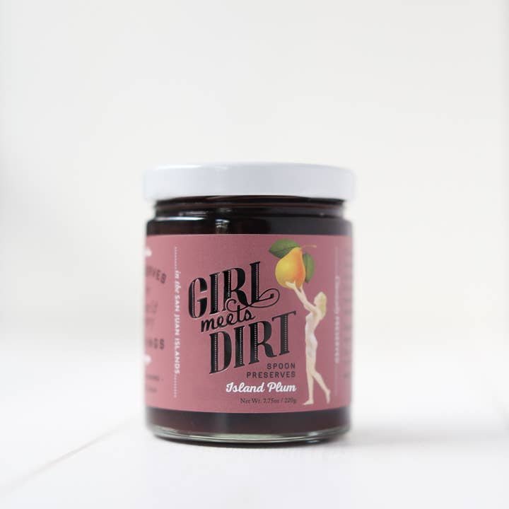A glass jar of Girl Meets Dirt Spoon Preserves, featuring a pink label with a woman holding a large fruit.