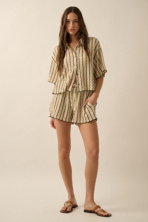 A woman wears Promesa USA Striped Textured Knit Drawstring Shorts with a matching beige, short-sleeve, button-up shirt featuring black stripes and lettuce-edge hems, paired with brown sandals against a plain background.