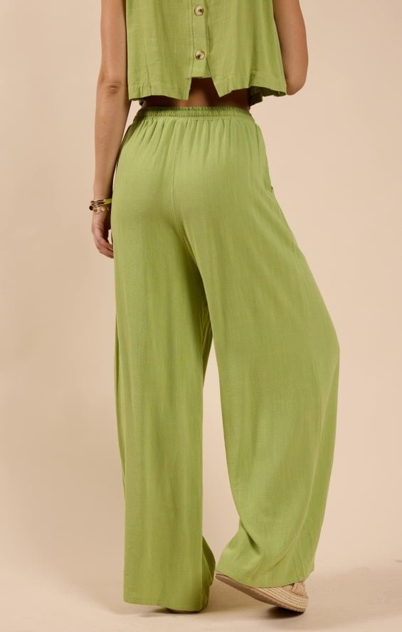 Woman models the Sugarloaf Elastic Waist Pants by Sadie And Sage in light green with a matching sleeveless top, featuring a soft polyester spandex lining, shown from the back against a neutral background.