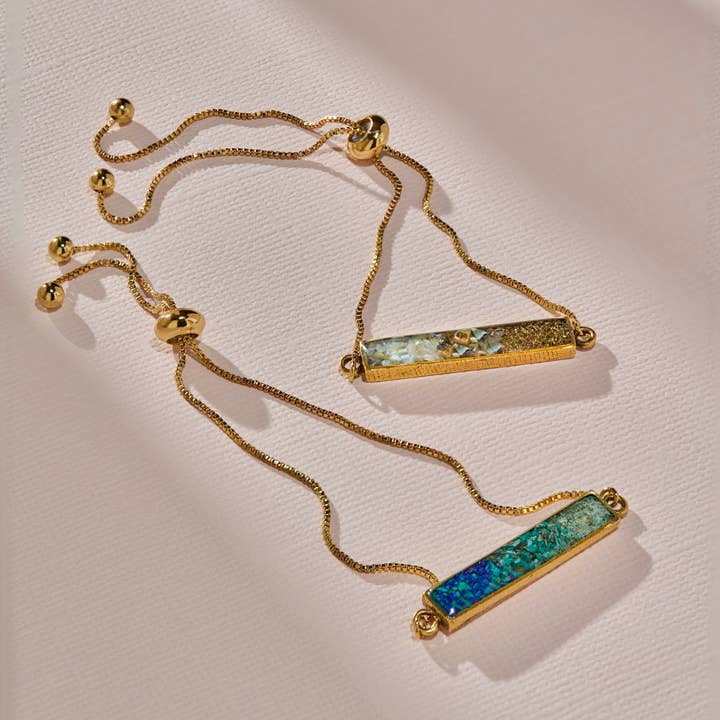 The Colorblock Ombre Adjustable Bracelet by cameoko features gold-plated, adjustable bands with rectangular multicolored inlay bars, creating a chic colorblock ombre effect. Displayed on a light pink textured surface.