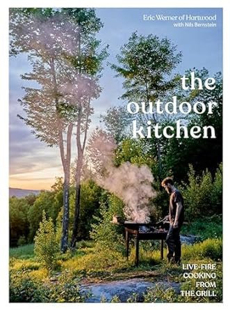 A person grills on an outdoor barbecue amidst trees, smoke rising against a scenic backdrop. The cover text reads "The Outdoor Kitchen | Penguin"—ideal for fans of wood fire cooking by Penguin.