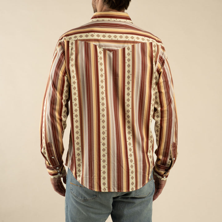 Someone is seen from the back wearing The Wyatt Pearl Snap long-sleeve western shirt by Sendero Provisions Co., featuring vertical red, beige, and brown stripes, paired with light blue jeans.