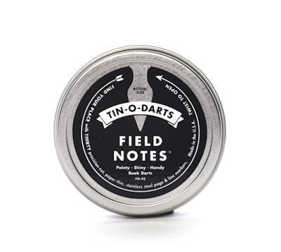 The Field Notes Tin-O-Darts is a round metal tin filled with stainless steel book darts, ideal as slim, reusable page markers—displayed on a white background.