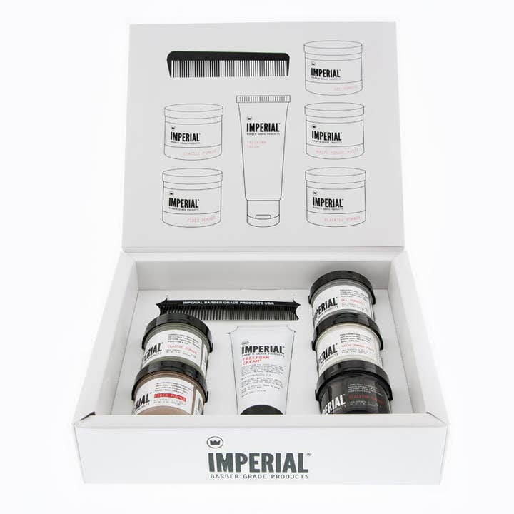 Open box showing the Travel Assortment by Imperial Barber Products—includes travel-size pomade jars, a tube, comb, and an illustrated product guide on the inside lid.