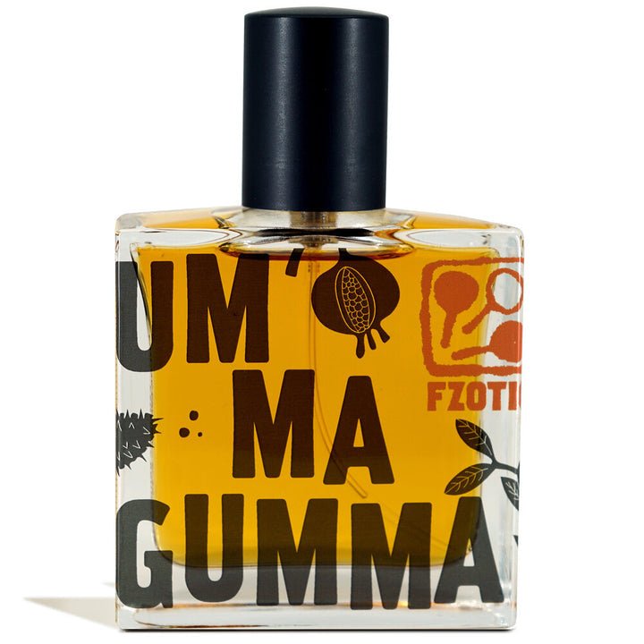 A clear glass perfume bottle labeled "Ummagumma | Fzotic" features a black cap, orange liquid, and striking black and orange graphics, suggesting an adult gourmand scent with dark chocolate notes for a sophisticated appeal.