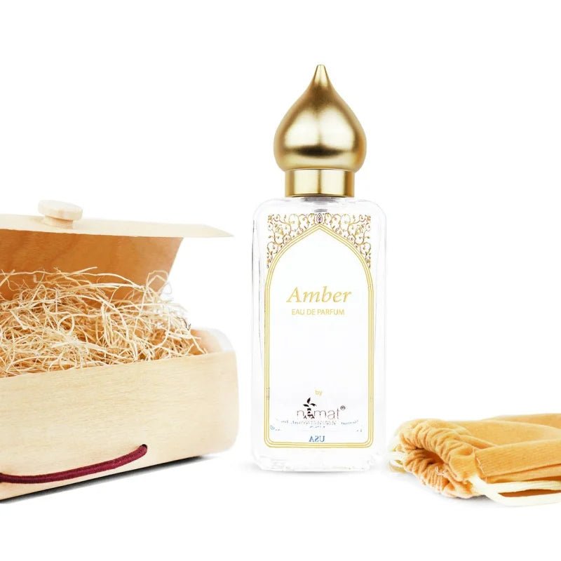 The Amber Eau de Parfum Spray 50ml by Nemat rests beside a wooden box with straw and a golden fabric pouch, perfectly reflecting the captivating essence of amber.
